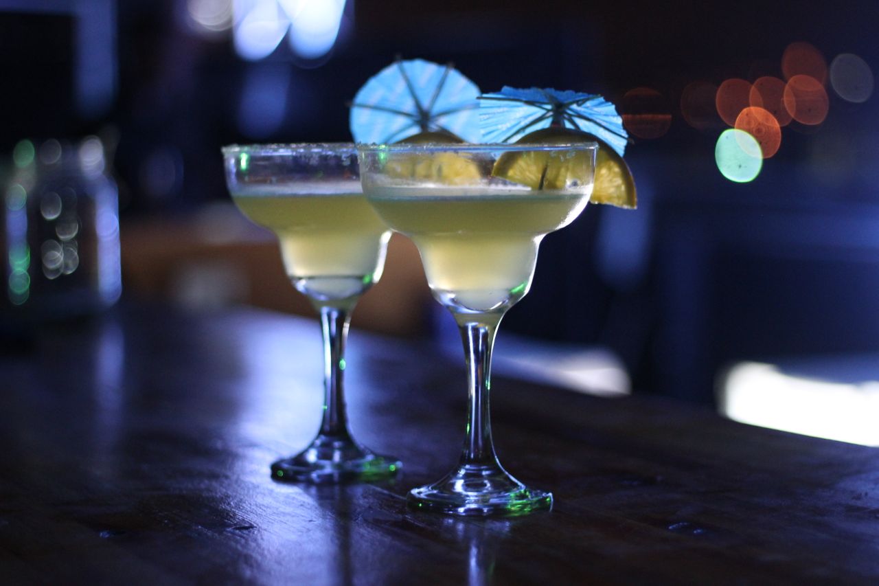 Two cocktails with lime and umbrellas on a dimly lit bar counter, perfect for nightlife.